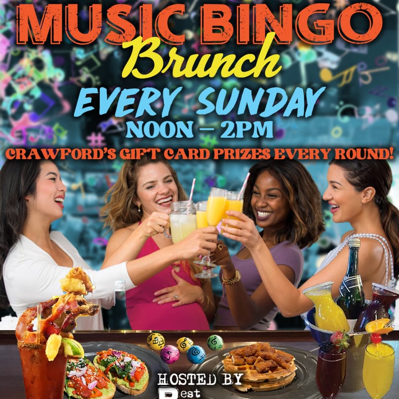 Four women toasting drinks at a lively brunch with food and drinks on the bar.