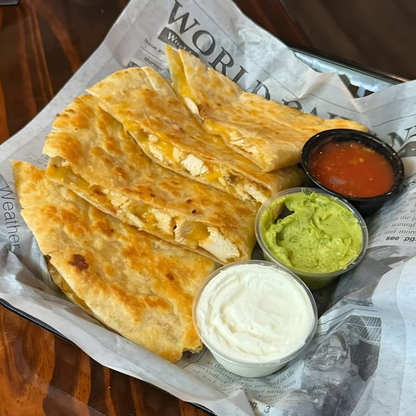 Chicken quesadillas with sides of salsa, guacamole, and sour cream on newspaper-lined tray.