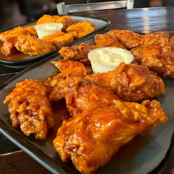 Two trays of saucy chicken wings with dipping sauce, ready to be served at Crawford's Corner.