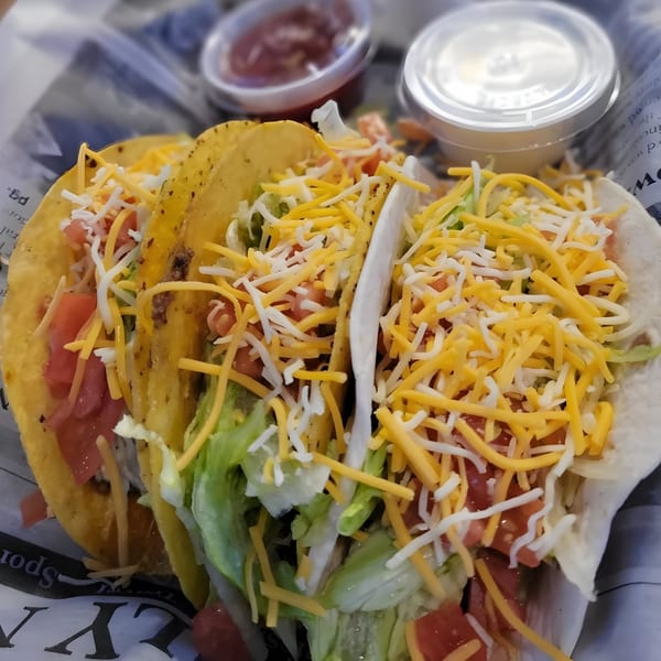 Three hard-shell and soft-shell tacos filled with meat, lettuce, tomatoes, and shredded cheese, with sauces.