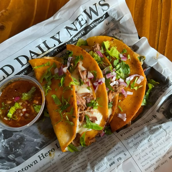 Three cheesy birria tacos with cilantro and red onion, served with a side of dipping sauce.